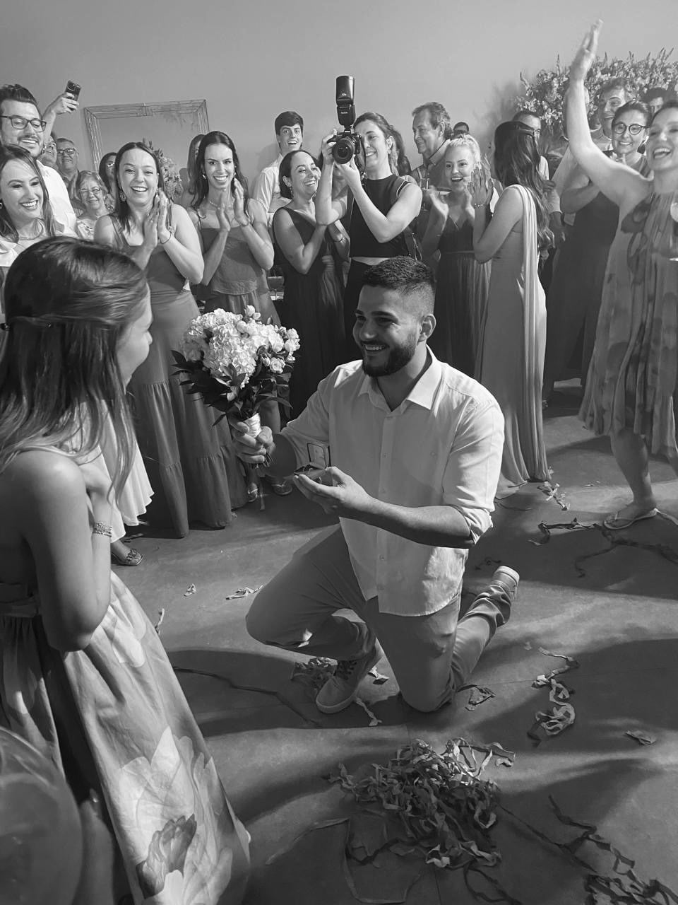 Edgar ajoelhado entregando o anel a Maria Elisa, cercados de amigos